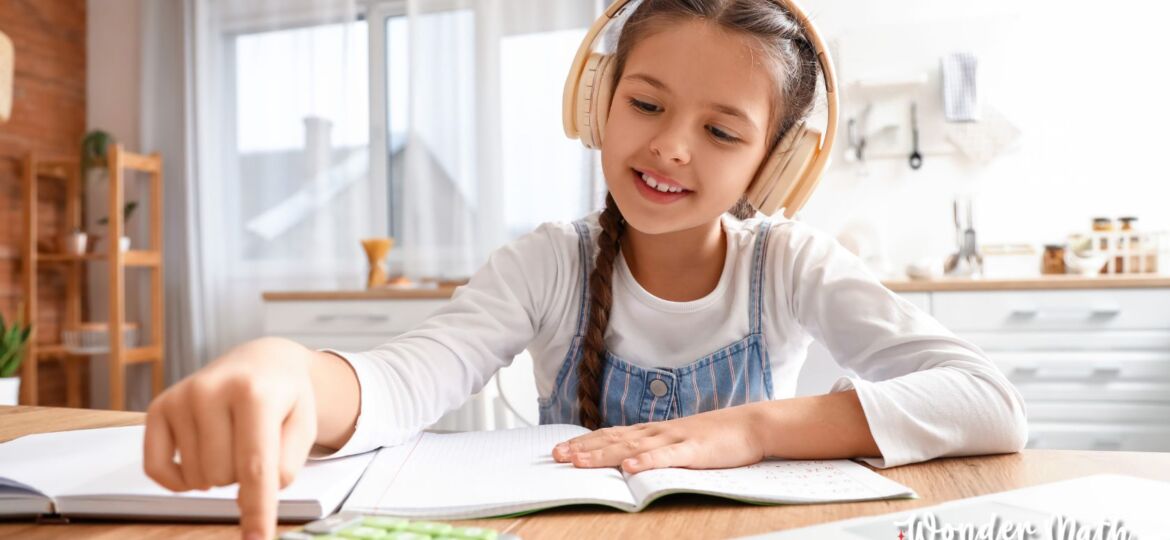 Picture of young girl doing math with her calculator and text books with headphones on.